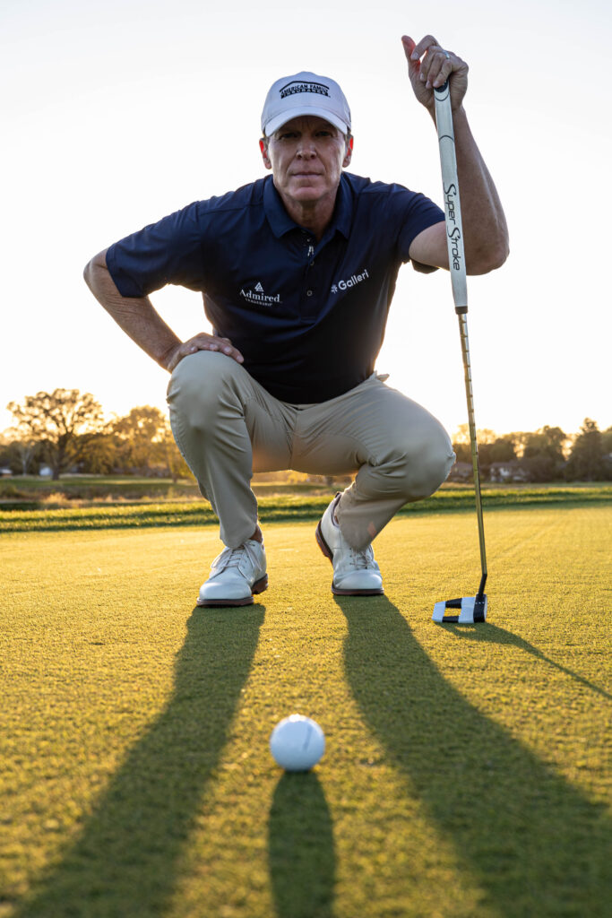 Steve Stricker crouches down, holding a putter.