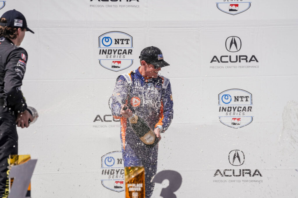 Scott Dixon rocía una botella de champaña de gran tamaño para celebrar el haber ganado su carrera.
